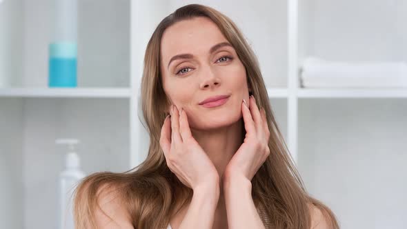 Positive Blonde Woman Applying Rejuvenation Cream on Face Smooth Skin