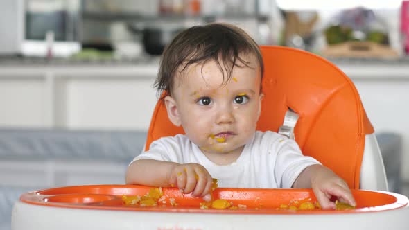 Funny Grubby Kid Indulges in a Baby Chair for Feeding in the Kitchen During Lunch Eats His Own Food