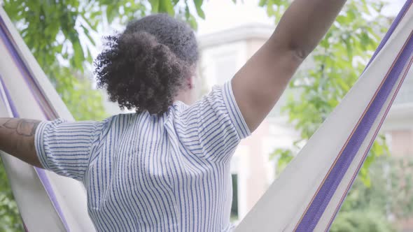 Back View of Young African American Woman Sitting in the Hammock, Relaxing in the Backyard