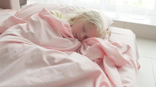 Adorable Blonde Girl Sleeping Sweetly in the Morning on Pink Bed Linens at Home