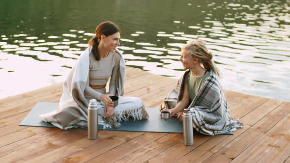 Female Friends Drinking Tea and Chatting on Lake Pier