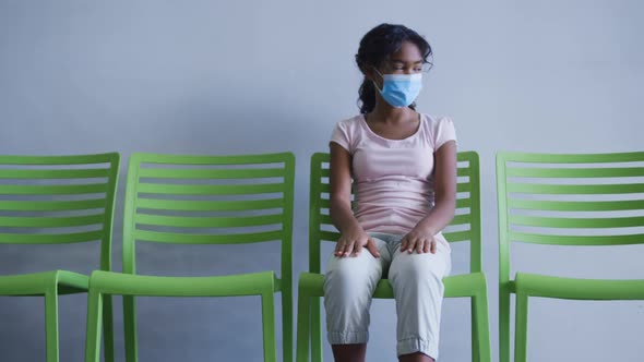 African american girl wearing face mask sitting on a chair at hospital