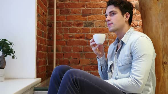 Pensive Young Man Drinking Coffee From Cup Loft Interior