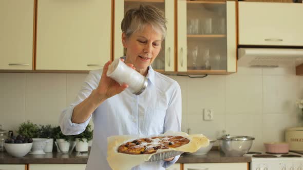 Senior woman sprinkling freshly baked tart with powdered sugar