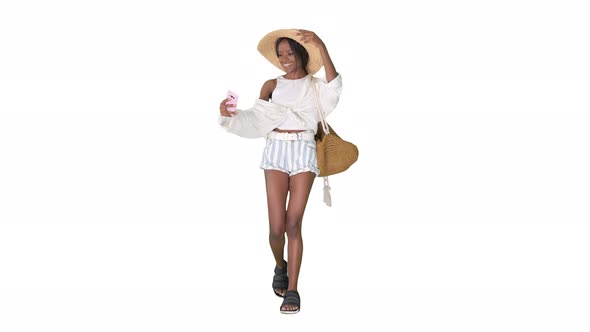 Smiling African American Woman in a Straw Hat Taking Selfie While Walking on White Background.
