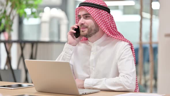 Arab Businessman with Laptop Talking on Smartphone in Office