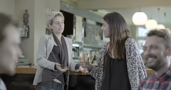 Woman talking and smiling with another woman while sitting in pub