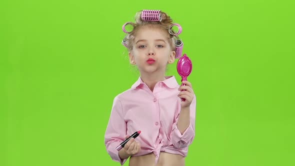 Child in Curlers Holds a Mirror in Her Hands and Paints Lipstick with Lipstick. Green Screen. Slow