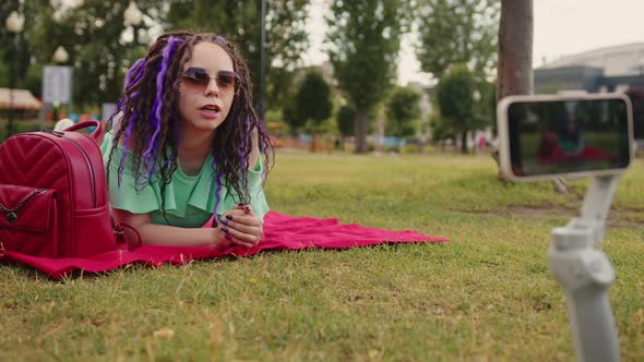 A female blogger shoots a video on a camera on a tripod on a sunny summer day