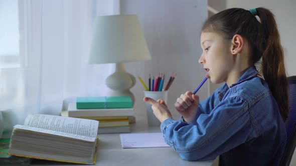 Little School Girl Chewing Pen and Counting on Fingers while Doing her Homework