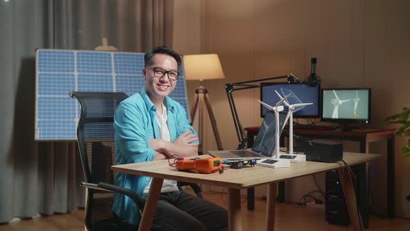 Asian Man Look At Wind Turbine , Cross Arms, And Smile To Camera While Working With Laptop