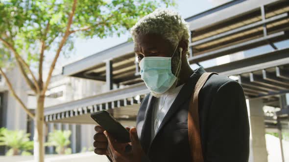 African american senior man wearing face mask using smartphone in corporate park