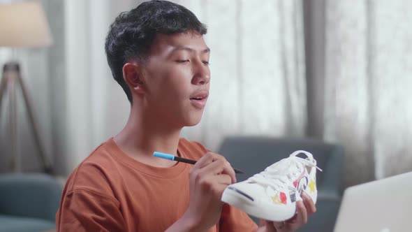 Asian Boy Footwear Designer Looking At A Laptop And Putting Coloured Unique Patterns On Sneakers