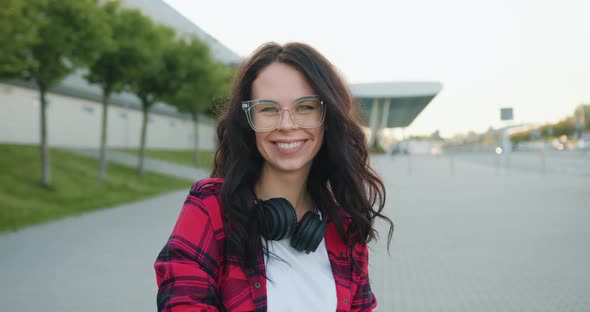 Brunette with Long Wavy Hair in Glasses and with Headphones Around Her Neck which Poses