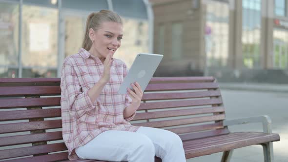 Young Woman Celebrating Online Win on Tablet While Sitting Outdoor on Bench