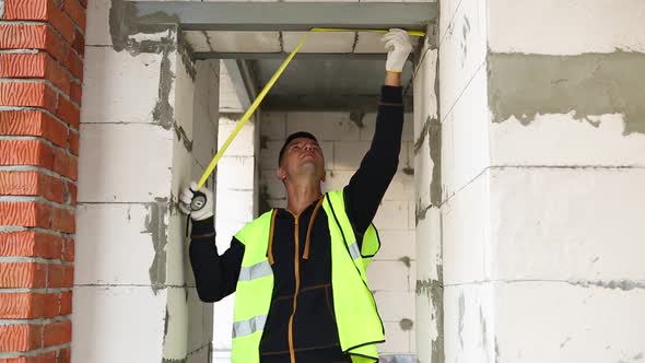 Construction worker at construction site measures the length of the window opening