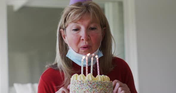 Senior Caucasian woman spending time at home, sitting in her living room blowing candles on birthday