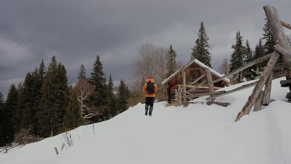 Walking Tourist Man Equipped Through the Snow to Amazing Wooden House in Countryside in the Middle