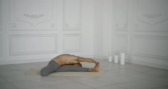 Flexible and Plastic Male Yogi with a Beard Doing Yoga on a Rug in a Bright Studio