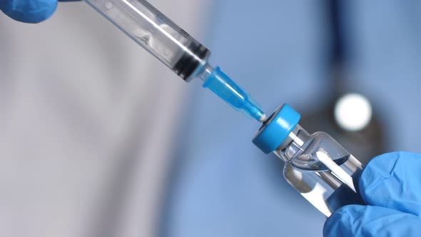 Doctor in Blue Latex Gloves Fill in Syringe with Vaccine From Glass Vial Closeup