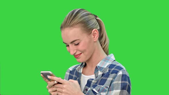 Young Woman Smiling While Texting a Message Via Cell Phone on a Green Screen, Chroma Key.