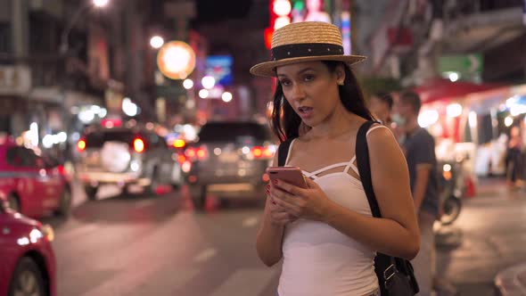 Young Brunette Woman Using a Mobile Phone Hail a Taxi at Night on Downtown Street