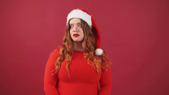 Young Plus Size Lady in Santa Hat Looking Around Gesturing Thumbs Up and Smiling Approval Gesture