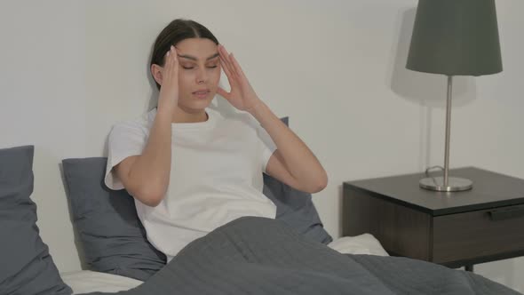 Hispanic Woman having Headache while Sitting in Bed