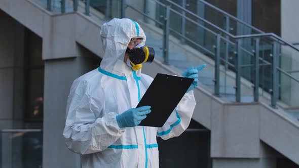 A Portrait of a Young Man in a Protective Suit, Respirator, Gloves and Safety Glasses Holds a Folder