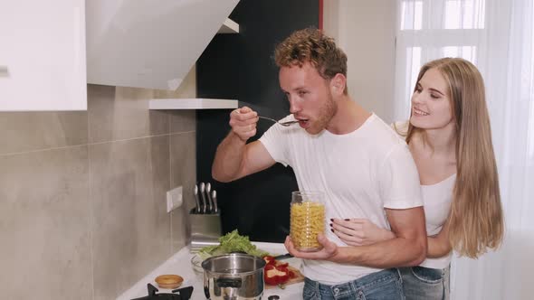 Happy Young Couple Embracing and Talking in the Kitchen While Cooking Breakfast at Home