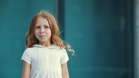 Active Little Girl in White Clothes and with Long Hair Stands in Front of Camera, Actively Moves