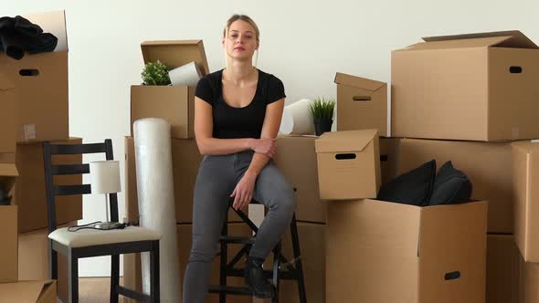A Moving Woman Sits on a Chair and Looks Seriously at the Camera in an Empty Apartment