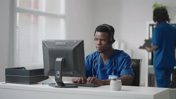 Afroamerican Male Doctor or Nurse with Headset and Computer Working at Hospital  alt