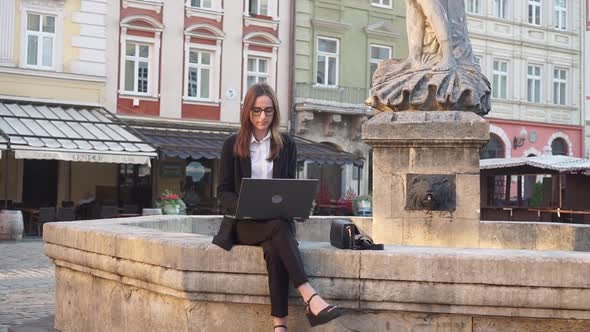 Young Girl Uses a Laptop Sitting Outside