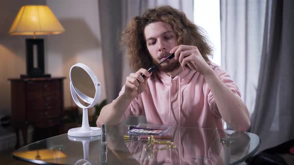 Middle Shot of Young Caucasian Man Opening Mascara and Looking at Brush. Male Intersex Person