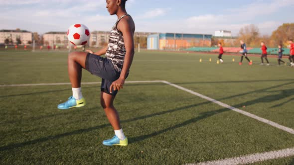 Young Black Girl in Soccer Training Juggles the Ball and Throws It From One Knee to Another