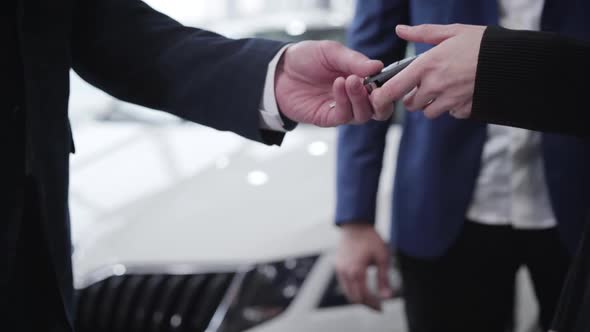 Close-up of Male Caucasian Hand Giving Car Keys To Unrecognizable Young Woman in Dealership. Wealthy