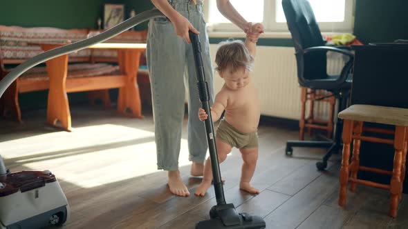 Mom and Baby Make Vacuum Cleaner Cleaning in Living Room As Mother and Child Play Game Indoors