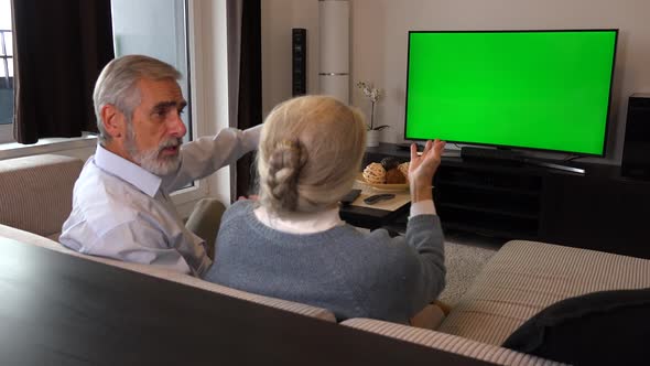 An Elderly Couple Sits on A Couch in A Living Room, Watches Tv with A Green Screen and Argues