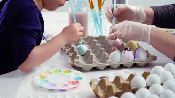 Little girl painting craft Easter eggs with acrylic paint.