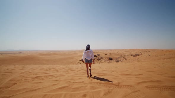 Young Woman in Jeans and White Shirt Walking Down Sand Dune in the Desert