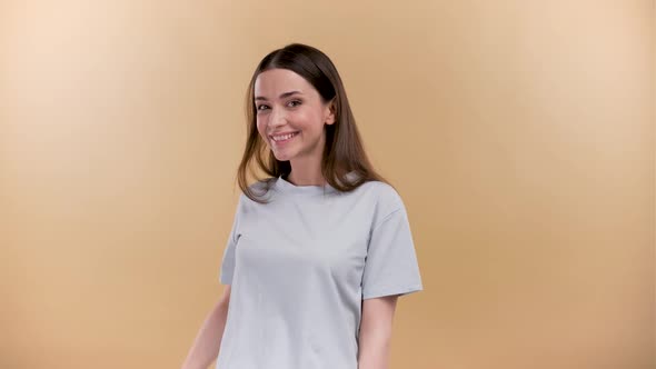 Happy Cheerful Young Girl Sending Kisses to the Camera on a Beige Background Wearing Neutral Clothes