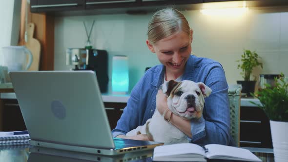 Smiling Woman Stroking and Hugging the Bulldog While Sitting at the Computer