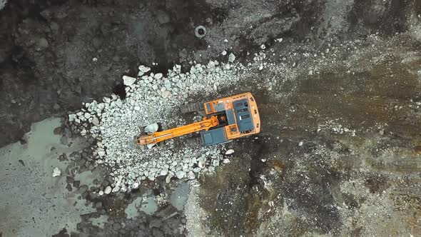 Large yellow excavator or bulldozer takes stones with bucket and fills hole.