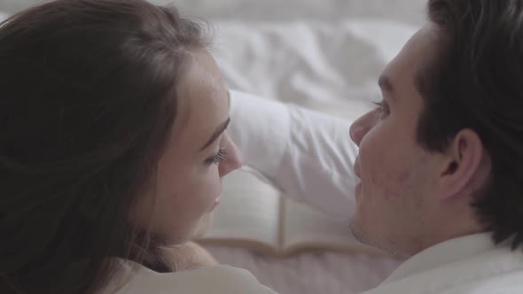 Top of Happy Young Couple Lying on the Bed Reading the Book Close-up. Handsome Man Touching Face of