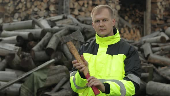 Lumberjack in Reflective Jacket. Man Woodcutter Hold Small Axe. Sawn Logs, Firewood Background