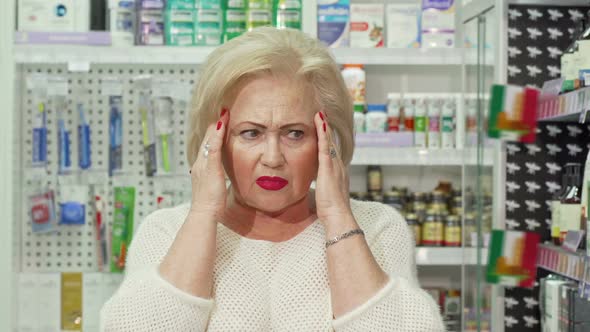 Senior Woman Having Headache, Looking for Medicine at Pharmacy