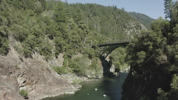 Slow pan to reveal a tall bridge over a river. Steep canyon surrounded by thick forest