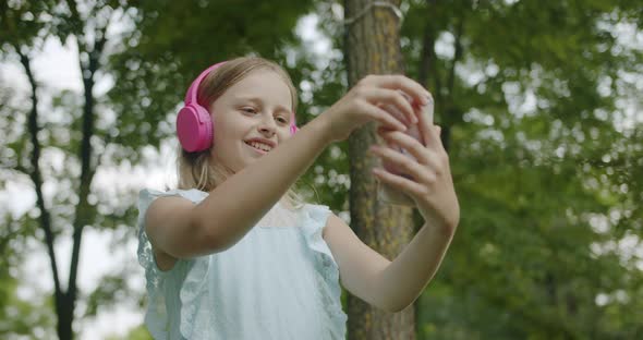 Teenager Listens to Music on Pink Headphones in Park Making Online Video Call