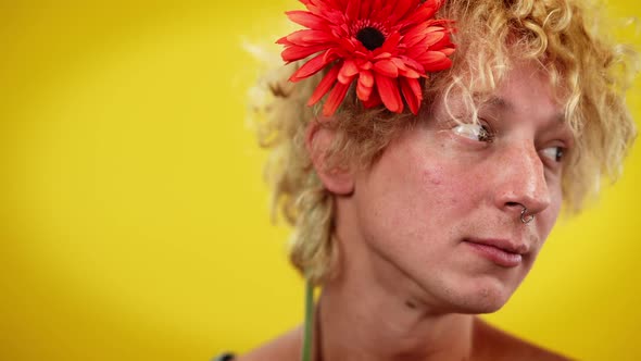 Sad Thoughtful Queer Man with Red Flower in Hair Posing at Yellow Background